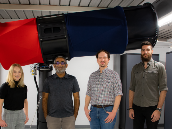 Vishnu Reddy and students standing in front of a telescope used in their research.
