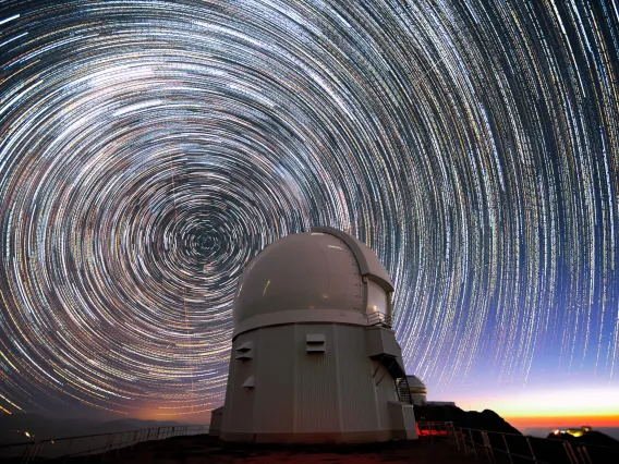 This long-exposure image, taken shortly before sunrise, shows stars appearing to “trail” around the south celestial pole (at the center of the circles) above the Southern Astrophysical Research Telescope (SOAR Telescope)