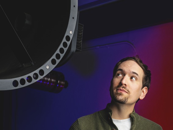 Photo of Adam Battle next to a telescope.