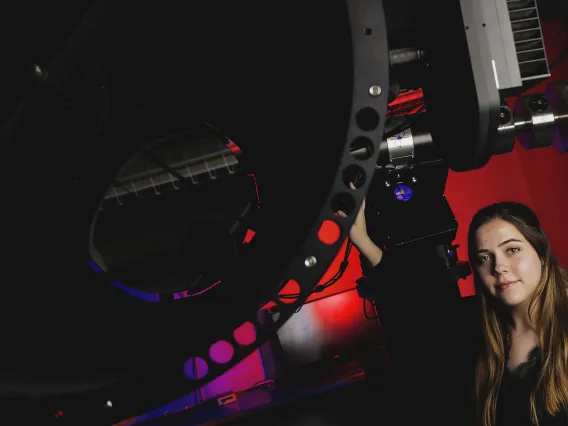 A photo of a student next to a telescope.