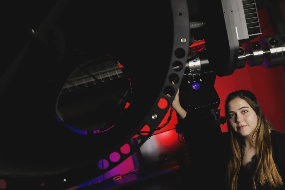 A photo of a student next to a telescope.