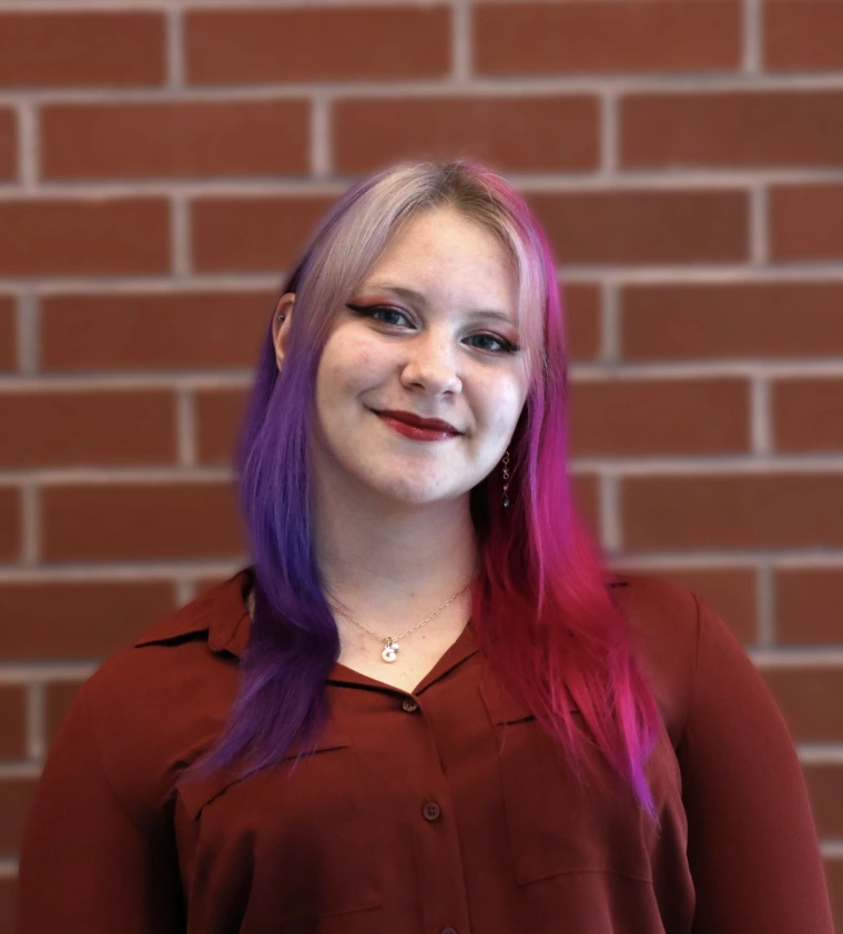 Student with shoulder-length blonde, purple and pink hair and smiling at the camera