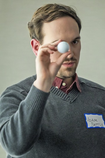 Photo of Adam Battle holding a golf ball to demonstrate the size of space debris he is researching.